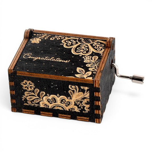 Enchanted Music Boxes hand-crank music box in black plywood with gold folk art floral engravings and Congratulations text.