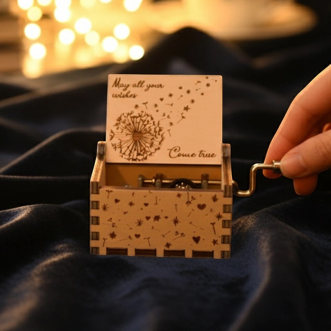 Enchanted Music Boxes plywood hand-crank music box with dandelion, heart, and star engravings on a dark blue fabric.