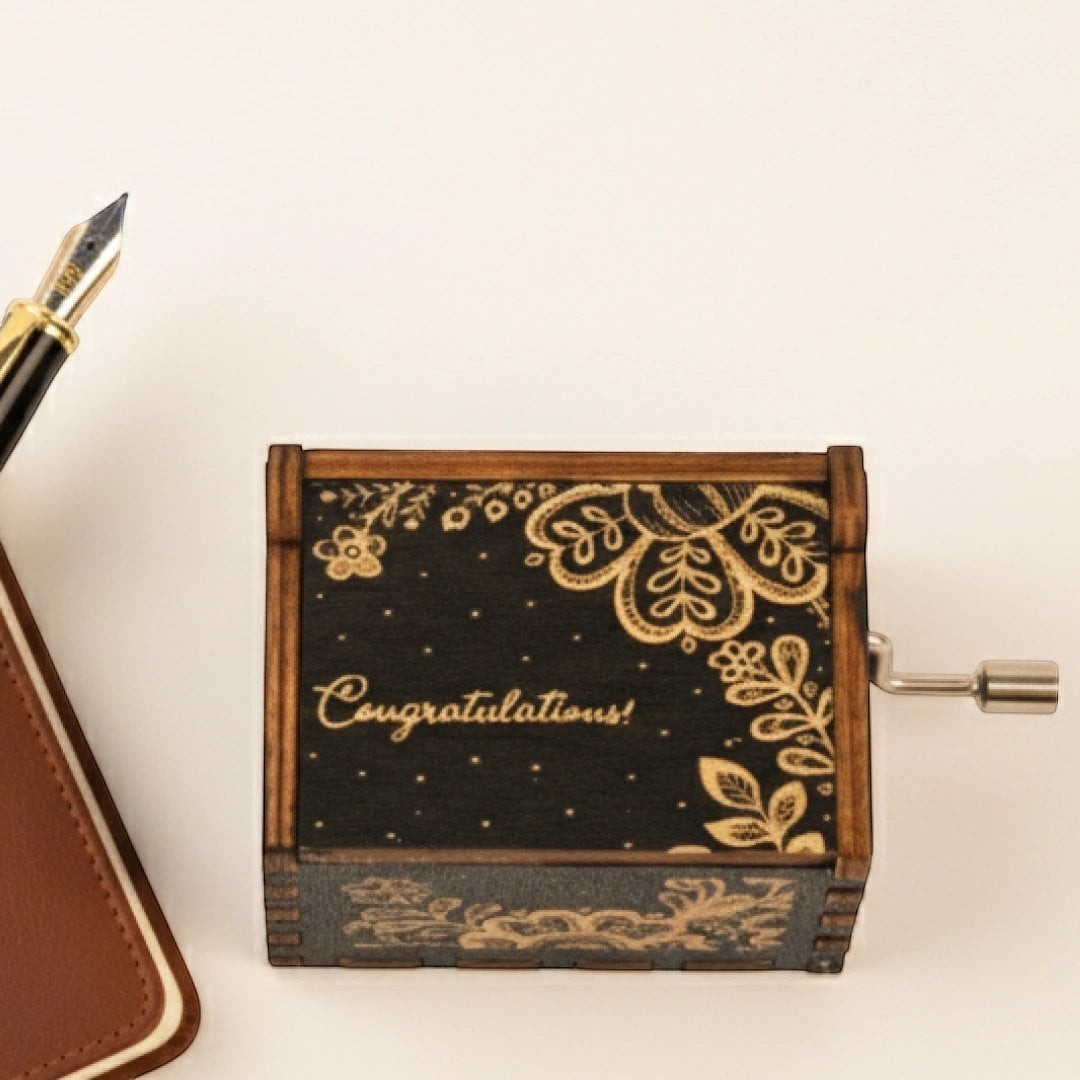 Enchanted Music Boxes hand-crank music box in dark wood with engraved folk art flowers and Congratulations text
