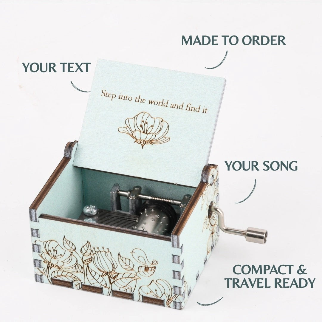 Enchanted Music Boxes hand-crank music box in light blue plywood with floral engravings and custom lid text.