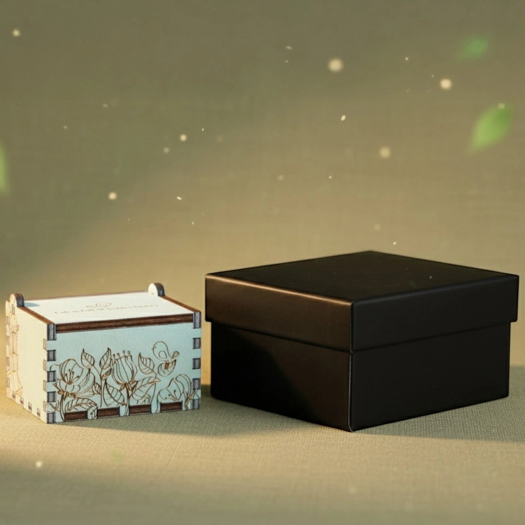 Enchanted Music Boxes plywood hand-crank music box with bird and floral engraving next to a black gift box.