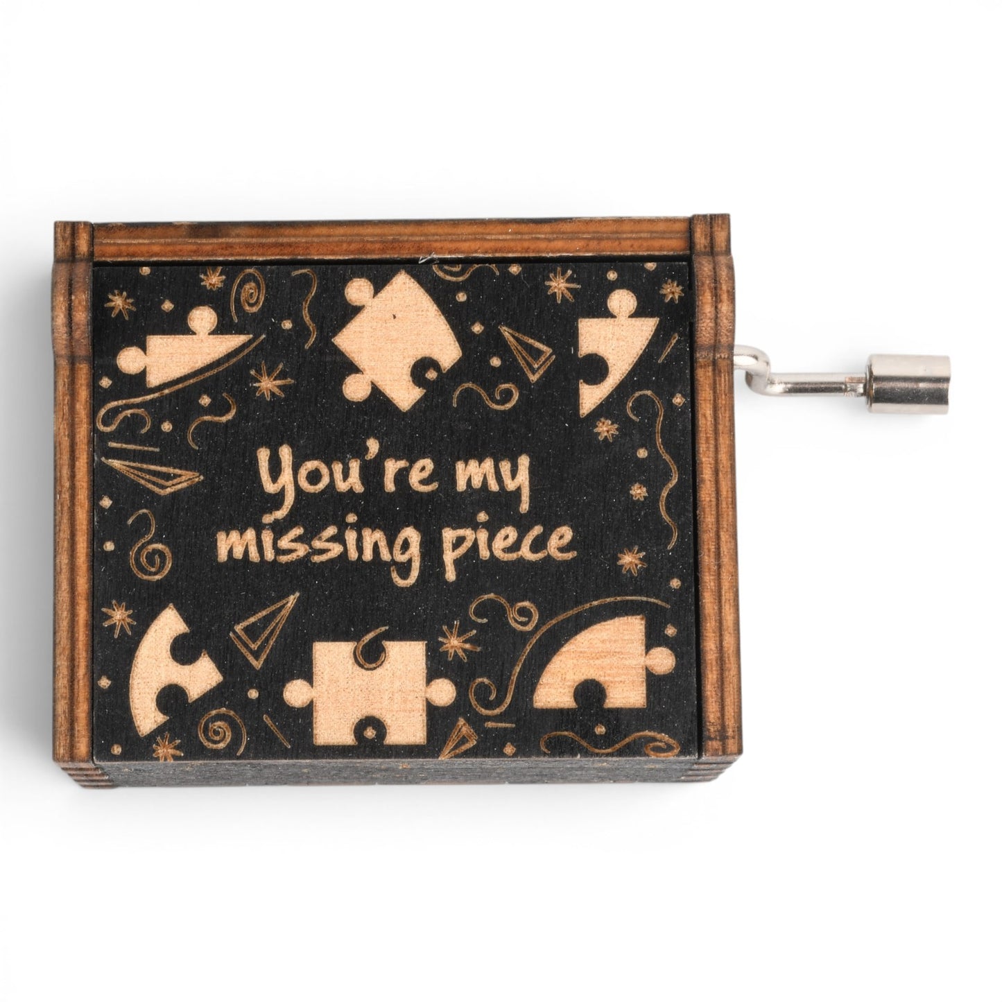 Enchanted Music Boxes plywood hand-crank music box with a black lid featuring puzzle piece engravings and text.