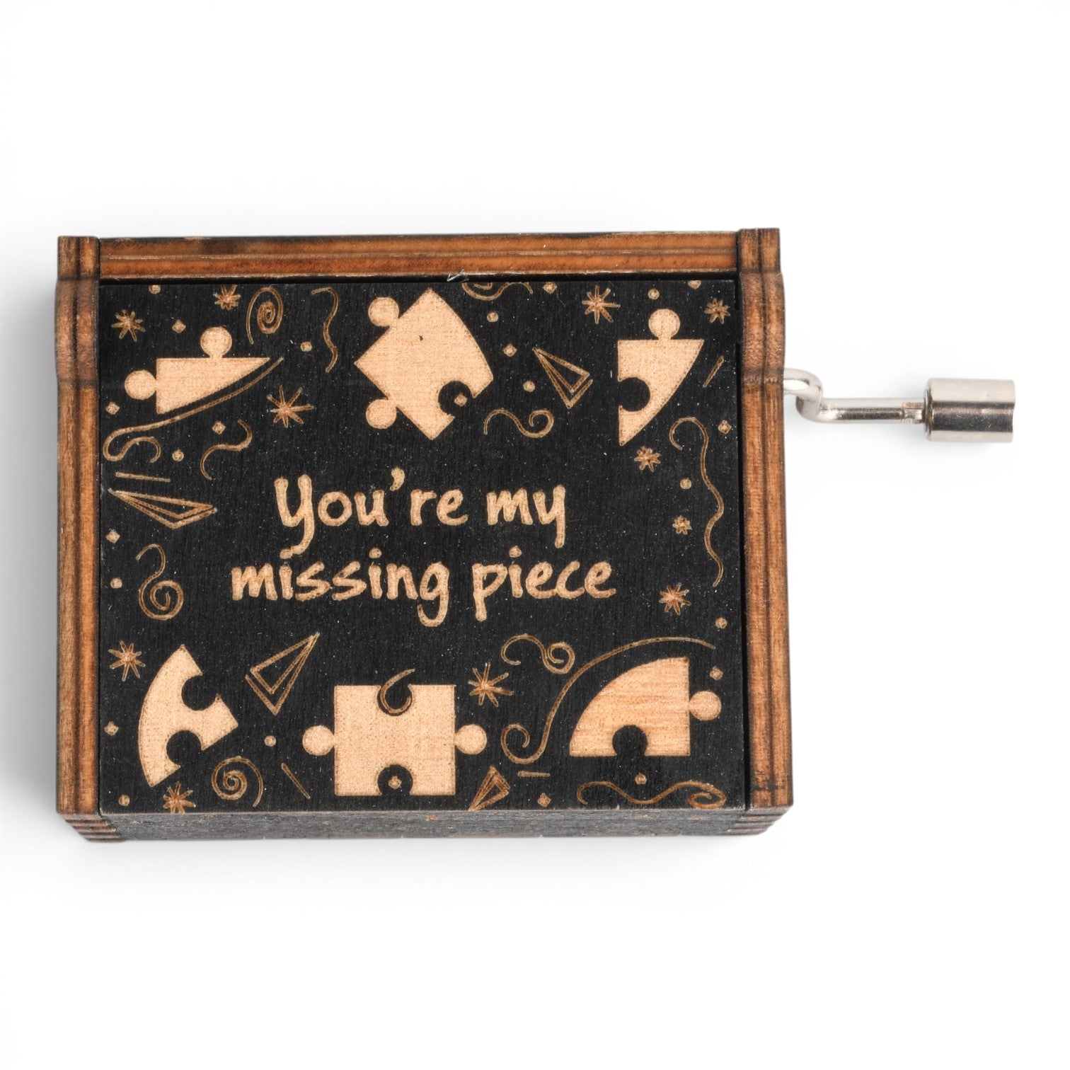 Enchanted Music Boxes plywood hand-crank music box with a black lid featuring puzzle piece engravings and text.