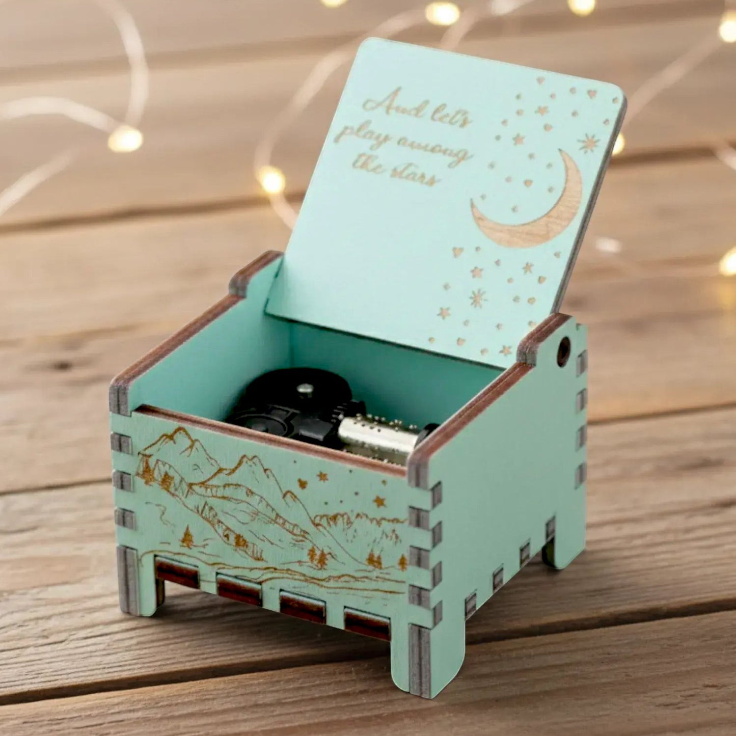 Enchanted Music Boxes wind-up music box in light blue wood with engraved moon, stars, and mountain landscape design.